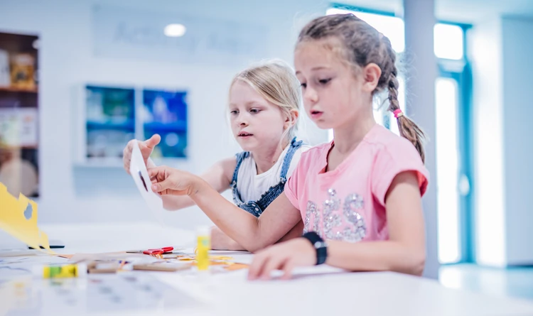 Sch&uuml;lerinnen schneiden Karton und kleben Materialien.